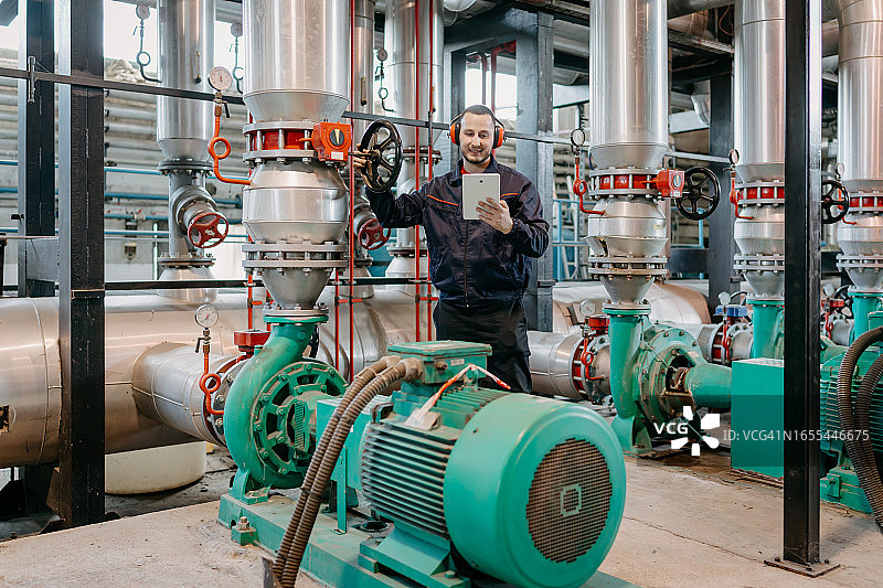 戴着安全帽的年轻白人男工程师正在转动管道系统上的轮子图片素材