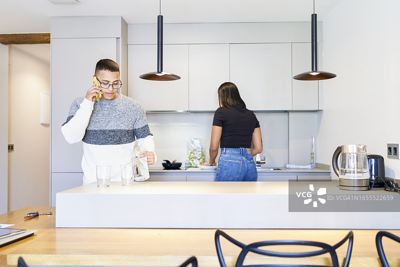 戴眼镜的男人在打电话，倒水，背景是一位正在做饭的短发女人图片素材