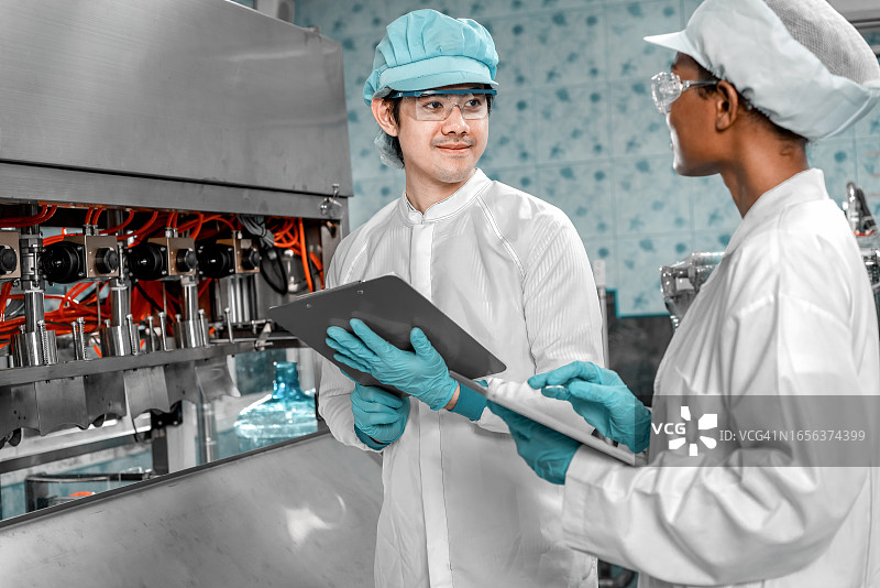 两名工人在饮料厂用笔记本电脑检查传送带上的产品。工人检查灌装线的处理情况。检验质量控制图片素材
