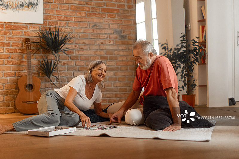美丽的老年夫妇坐在地板上，将拼图放在一起。图片素材