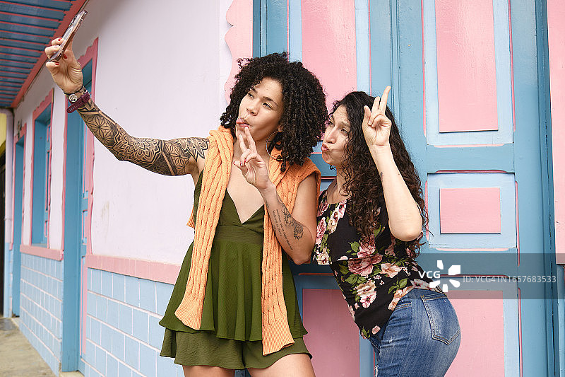 两个在录制视频时用手机比划的女人图片素材