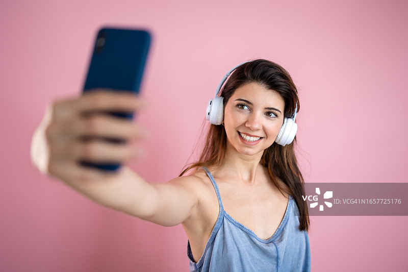 年轻微笑的女人在粉色背景下用手机自拍图片素材