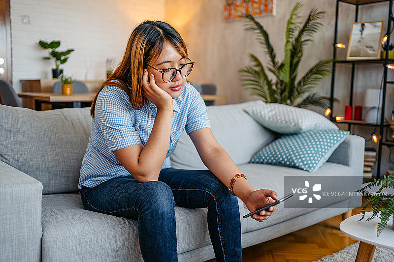 坐在沙发上玩手机的无聊女人图片素材