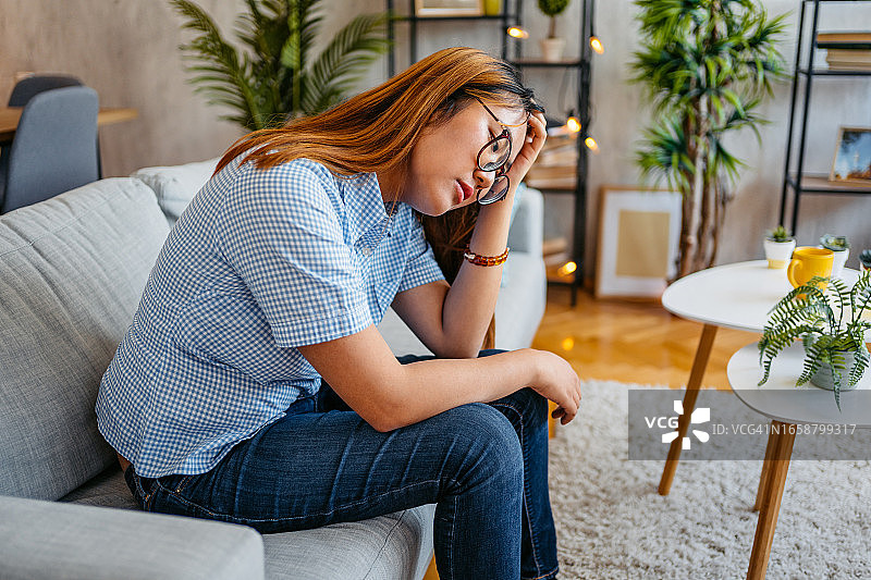 独自坐在客厅里，神情沮丧的年轻女人图片素材