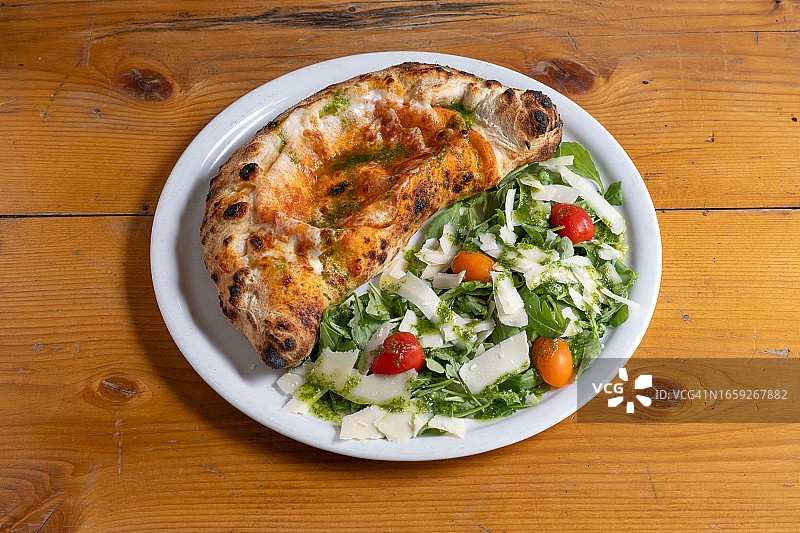 木桌上的意式卡尔佐内披萨和芝麻菜沙拉图片素材