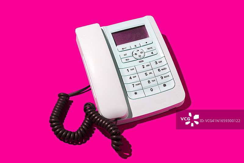 粉色背景上的白色复古电话与电话线：关于旧式电话、固话、通话、距离、收听、交换机和客户服务的概念图片素材