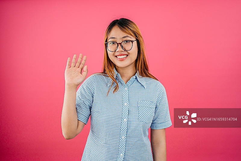 站在粉色背景前挥手的快乐年轻女人图片素材