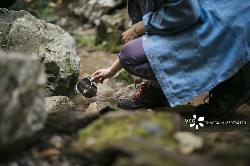 女游客在森林徒步旅行时，在山涧中清洗餐具的特写图片素材