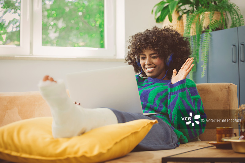 腿部受伤的年轻女人在家使用笔记本电脑图片素材