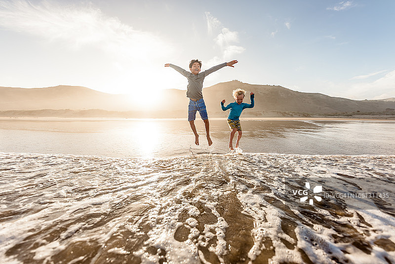 两个快乐的男孩在海滩上跳入水中图片素材