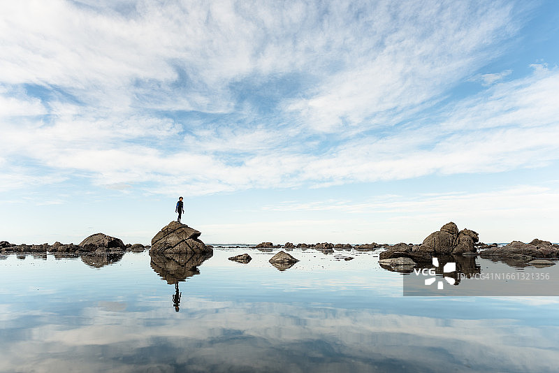 站在新西兰水边岩石上的青少年男孩图片素材