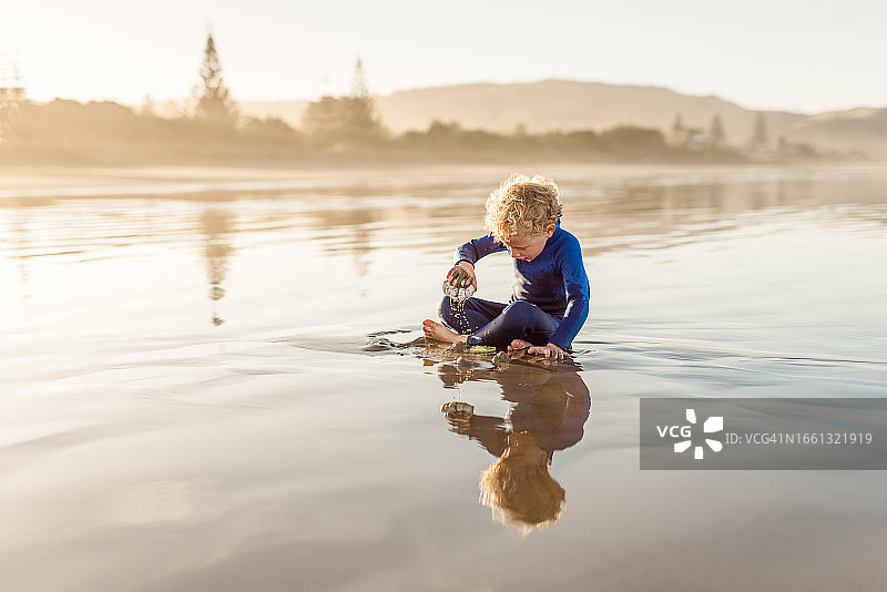 在海滩上玩沙子的卷发小男孩图片素材