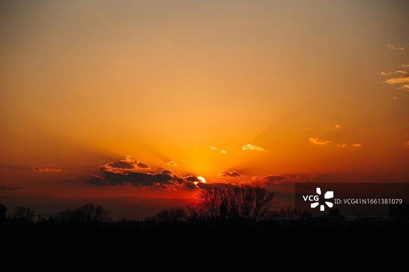 日出或日落时分，地平线后戏剧性的太阳与树木和建筑物图片素材