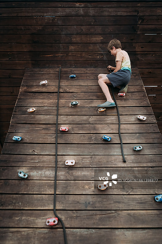 夏日里，孩子在操场上攀爬岩壁图片素材