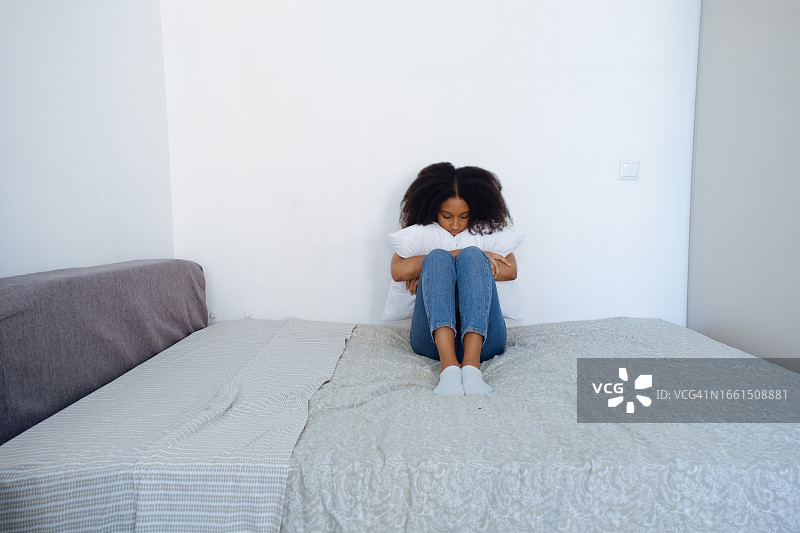 悲伤的女孩坐在卧室的床上，因离婚、堕胎、流产或争吵后感到沮丧和孤独。一个女人在反思严重的问题，一场危机。孤独、抑郁、情绪倦怠的概念图片素材