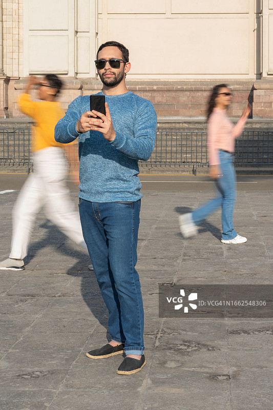 男子用手机自拍，背景是行人图片素材