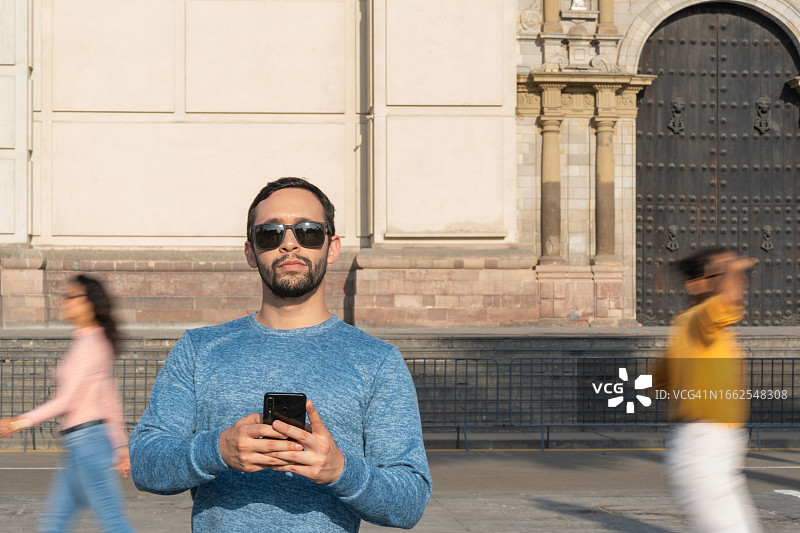 男人查看手机，身后有人走过图片素材