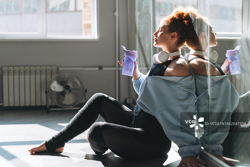 年轻红发女舞者在舞蹈室镜子前休息图片素材