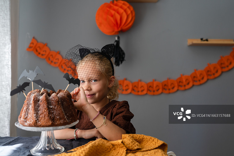 微笑的猫咪装扮女孩站在家里的万圣节蛋糕后面图片素材