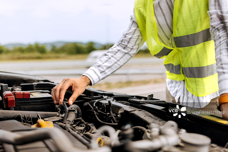 身穿反光背心的年轻男子查看高速公路上抛锚的汽车引擎盖图片素材