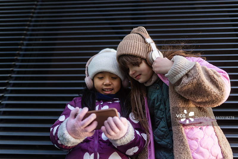 寒冷冬日城市里，小女孩用智能手机观看视频图片素材