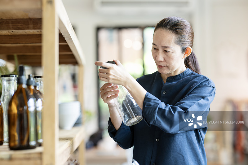 确保定价策略和产品质量支持盈利能力和长期业务增长：日本女性顾客在室内装饰品商店购物，并从展示架上挑选玻璃罐图片素材