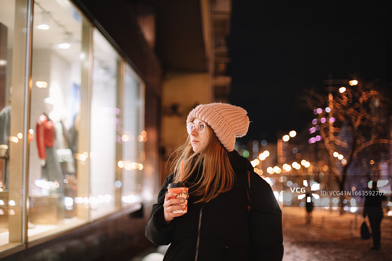 冬季，年轻女子走在城市街道上看商店橱窗图片素材