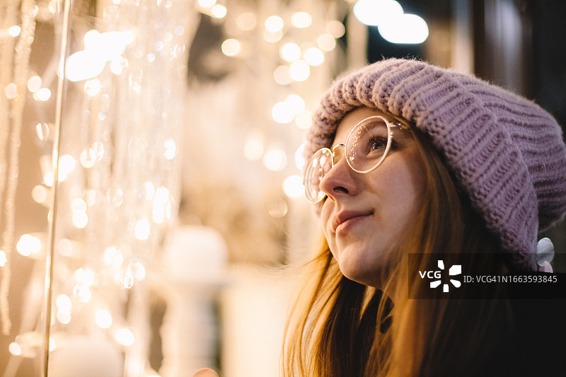 年轻女人看着装饰着圣诞灯的商店橱窗图片素材