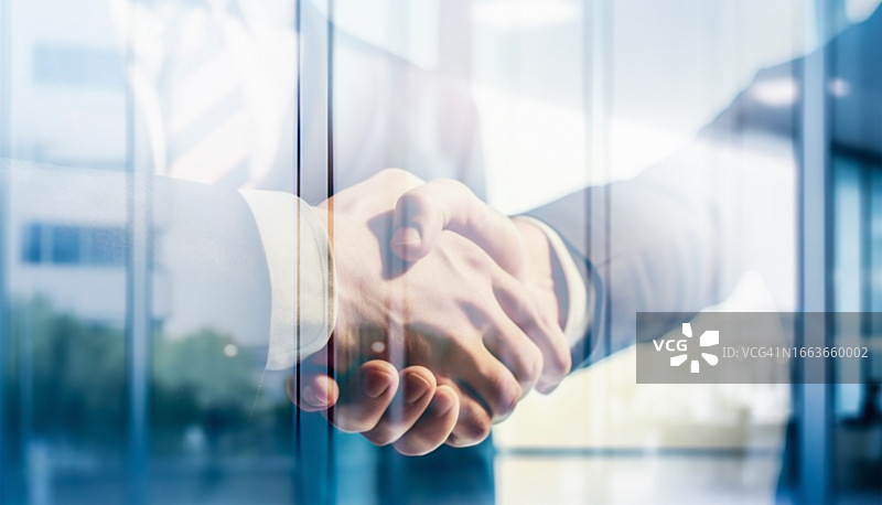 商人们握手，大型商业中心窗户倒影图片素材