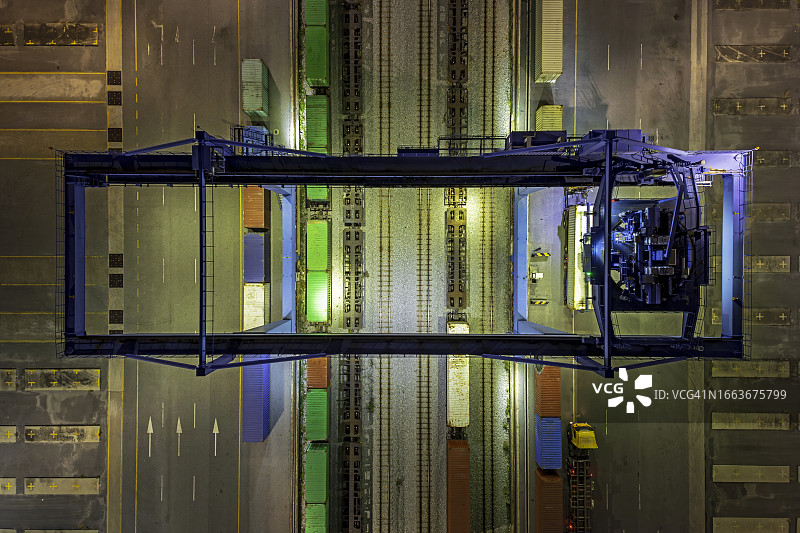 在码头商业港口，起重机将集装箱从火车卸到集装箱卡车的航拍俯视图图片素材