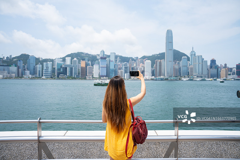 后视镜中拍摄的香港天际线和拍照的年轻女人图片素材
