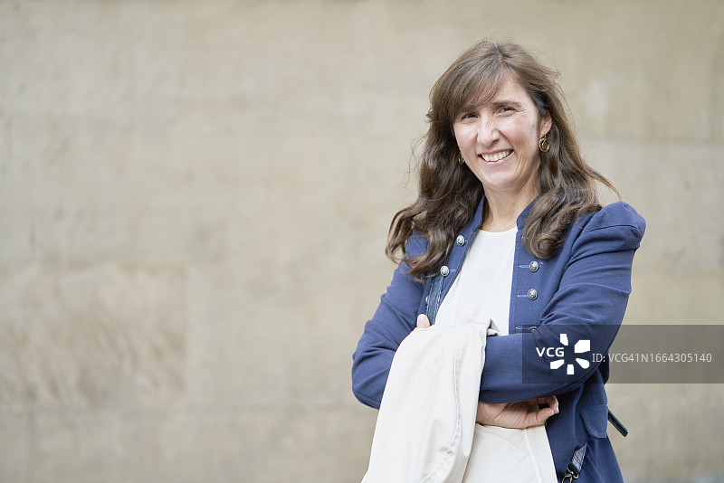 站在街上微笑看着镜头的女人，手拿外套，建筑外景正面照图片素材