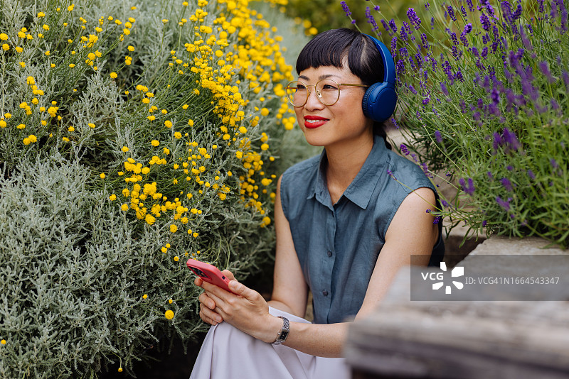戴着耳机，在户外用手机听音乐的快乐美丽亚洲女人图片素材