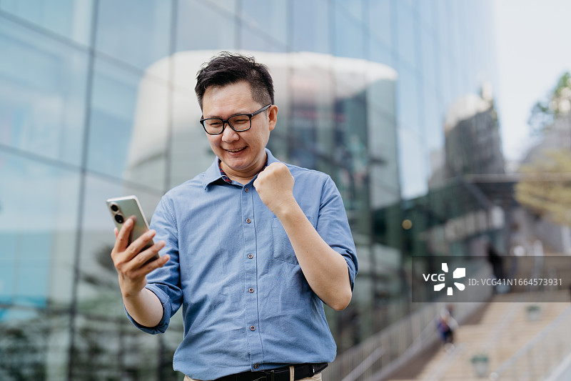 快乐的亚洲商人手持智能手机图片素材