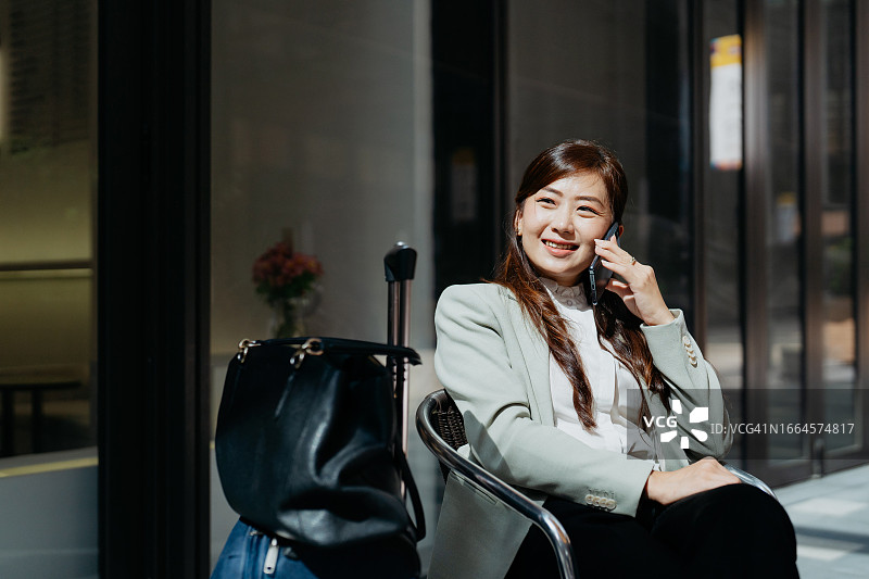 在路边咖啡馆用智能手机交谈的女性商务旅客图片素材