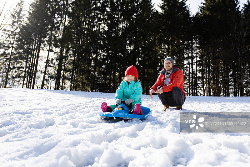 冬天，父亲推着坐在雪橇上的孩子图片素材