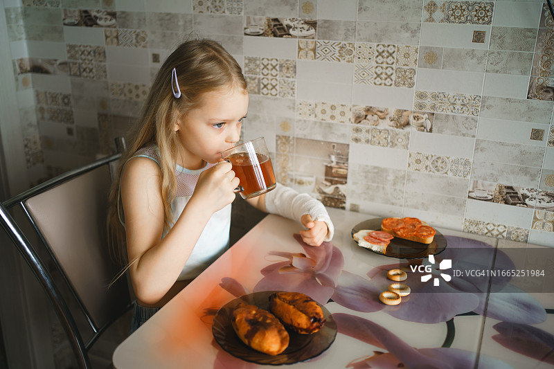 手臂打着石膏的女童在家喝茶图片素材