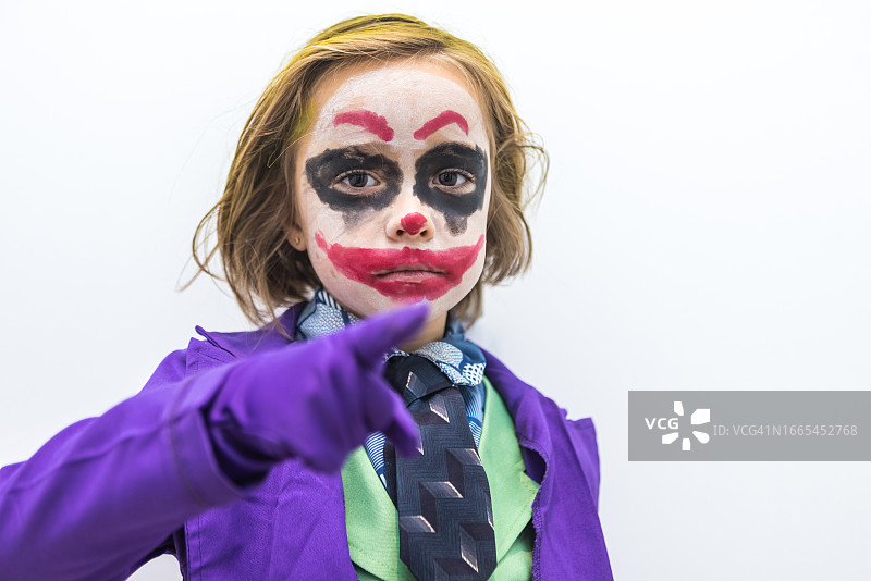 万圣节和嘉年华上装扮成邪恶小丑的女孩，在白色背景上指着手指。服装、怪物、疯狂、不死、亡灵节、庆祝和伪装概念图片素材