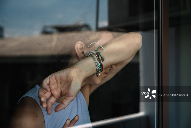 用一只胳膊遮住脸靠在酒店窗户上的女人，心理健康概念图片素材