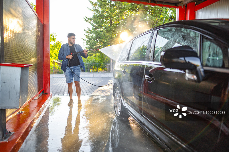 年轻男人在自助洗车场用水管清洗汽车图片素材
