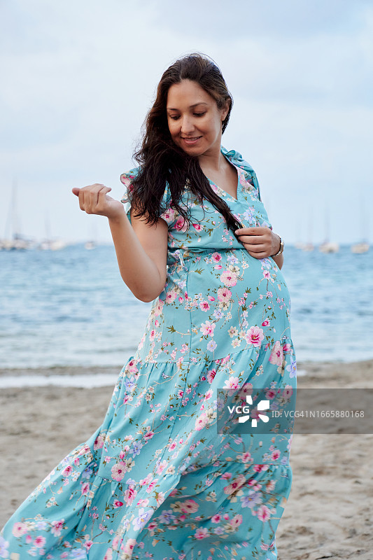 穿着连衣裙的孕妇站在户外海滩上图片素材