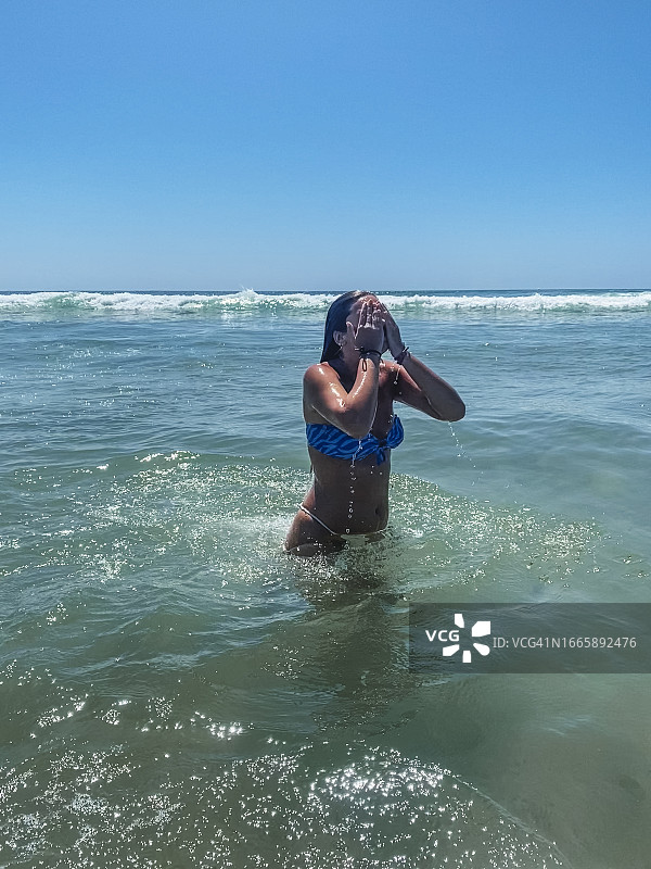 海滩上的年轻女子甩掉脸和头发上的水图片素材