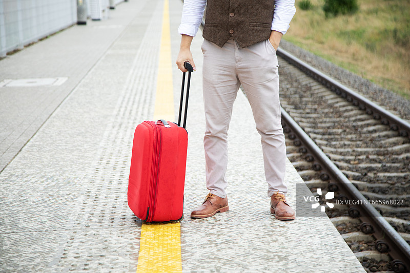 自信地站在站台上，手提红色手提箱的男子图片素材