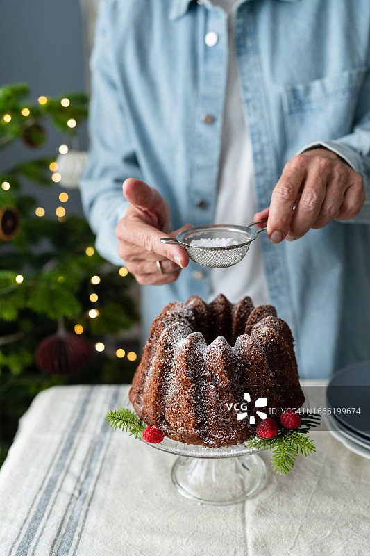 无法辨认的男人在圣诞节磅蛋糕上撒糖粉的手图片素材