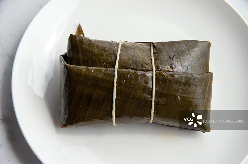 盘子里用玉米面、鸡肉、猪肉、青豌豆和洋葱包裹的蒸玉米粉蒸肉图片素材