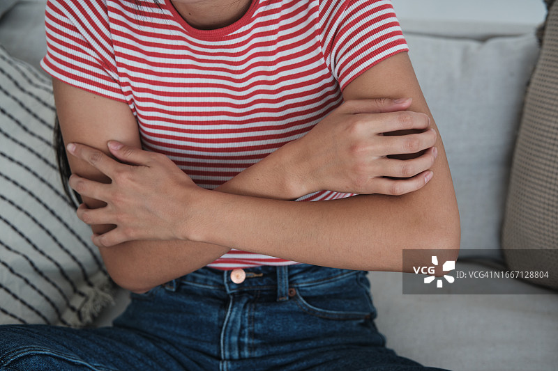 焦虑和瘙痒：紧张的女人坐在沙发上抓挠皮肤图片素材