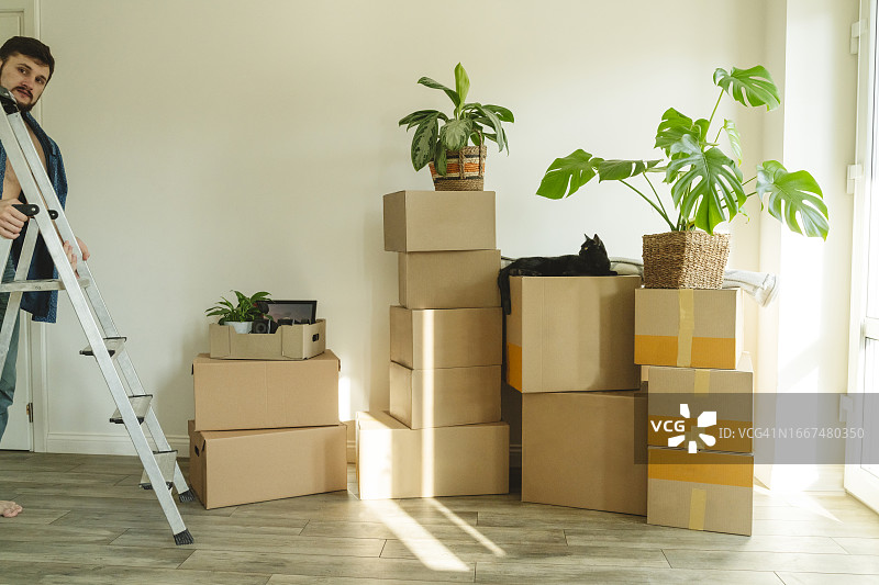年轻男人带着梯子站在新家的纸箱旁图片素材
