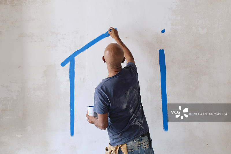 光头建筑工人在工地用画笔在墙上绘画图片素材