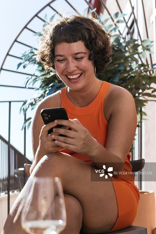 在阳台上，面带微笑使用智能手机的女人图片素材