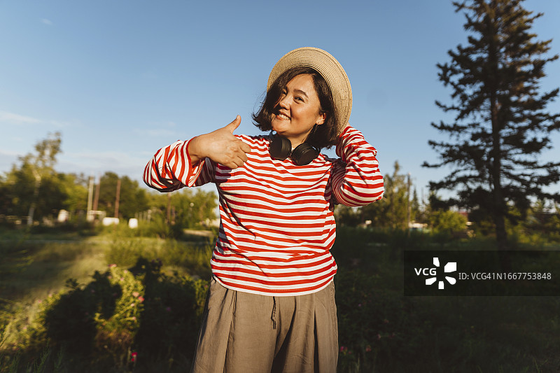 微笑的女人戴着帽子在田野里竖起大拇指图片素材